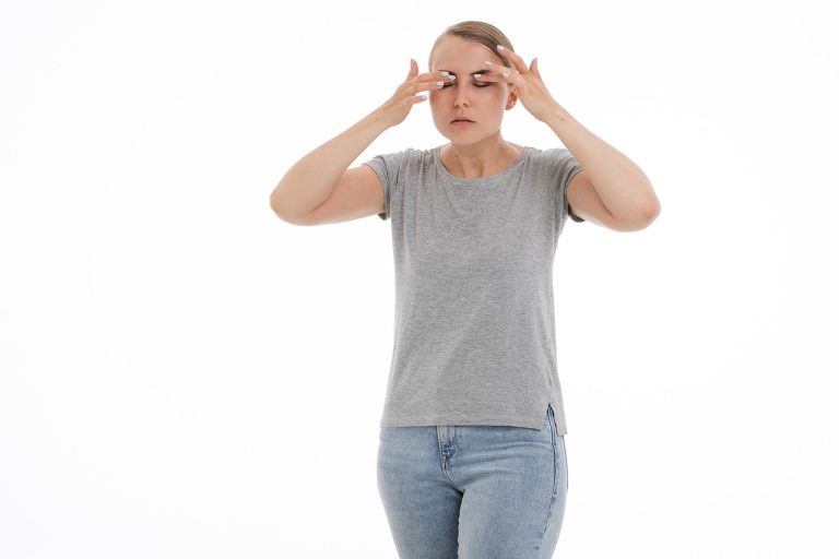 Mulher com camiseta cinza e calça jeans esfrega os olhos para tirar cisco do olho